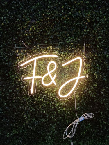 LED Neon Schild mit Initialen „F & J“ in warmweiß auf dunkler Pflanzenwand