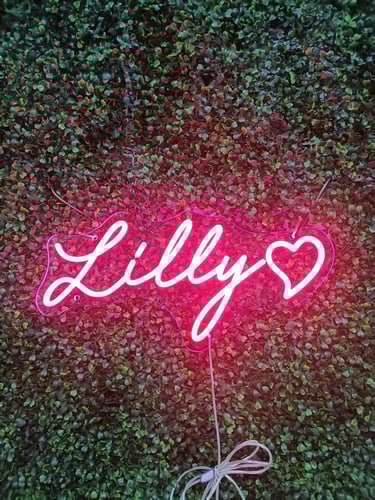 hellrosa LED Neon Schild mit Schriftzug „Lilly“ und Herz auf grüner Pflanzenwand