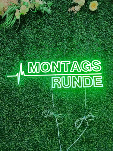 grünes LED Neon Schild „Montagsrunde“ mit Herzschlaglinie für Podcast auf Pflanzenwand
