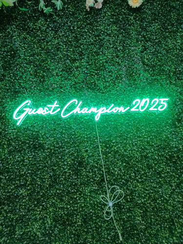 grünes LED Neon Schild mit Schriftzug „Guest Champion 2025“ auf grüner Pflanzenwand bei Event