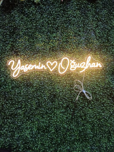 warmweißes LED Neon Schild mit Schriftzug „You and I“ und Herzsymbol auf grüner Pflanzenwand