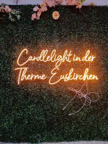 oranges LED Neon Schild mit Schriftzug „Candlelight in der Therme Euskirchen“ auf grüner Pflanzenwand