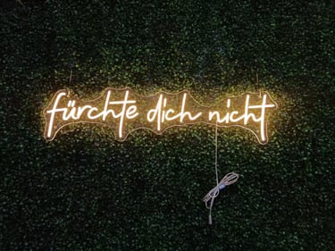 warmweißes LED Neon Schild mit Schriftzug „fürchte dich nicht“ auf grüner Pflanzenwand