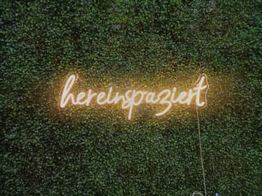 Warm Weißes LED Neon Schild hereingespaziert Schriftzug als dekoratives Neon Wandlicht auf grüner Pflanzenwand