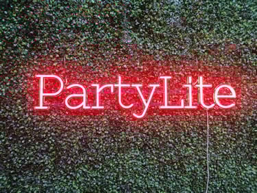 rotes LED Neon Schild PartyLite Schriftzug auf grüner Pflanzenwand als individuelles Firmenlogo Neon