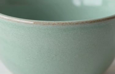 Close-up detail of a textured ceramic surface in #A4BC9F sage green, highlighting fine craftsmanship and material quality.