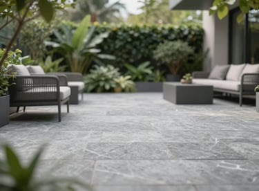 An outdoor terrace paved with durable stone-effect slabs in #F7F7F7, surrounded by lush greenery and minimalist patio furniture.