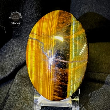 Polished oval tiger's eye healing stone with golden and brown chatoyant bands on a display stand.
