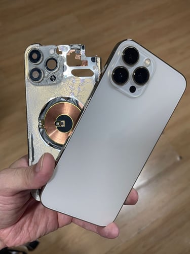 A person holding a damaged white iPhone next to its shattered back glass panel and MagSafe charging coil.
