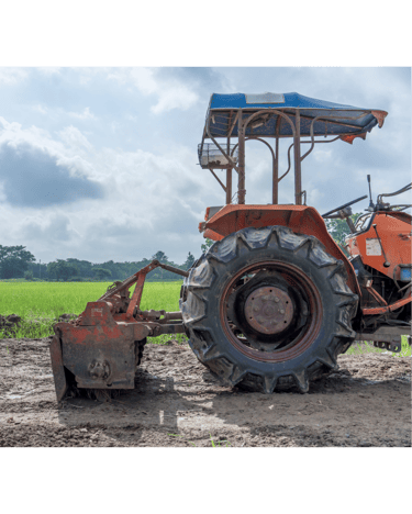 Orange agricultural campact tractor with a rotary tiller attachment parked in a muddy farm field.
