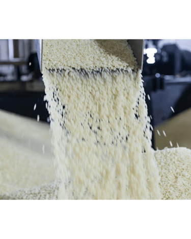 White long-grain rice falling from a metal chute in a commercial food processing facility.