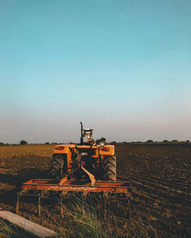 An orange farm tractor with a plow attachment stands in a tilled field under a clear blue sky.