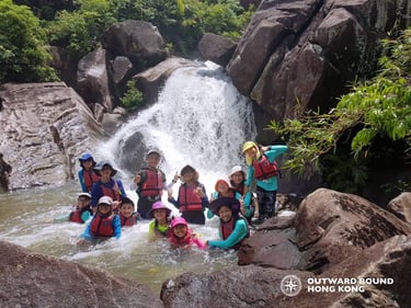 A diverse group of youth in life jackets enjoying an outdoor adventure at a Hong Kong waterfall.