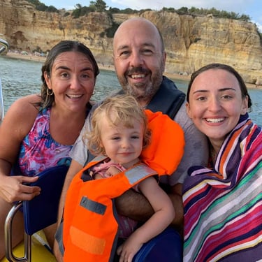 A smiling family of four enjoys a boat trip near the scenic cliffs of Algarve, Portugal.