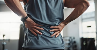 A man holding his lower back in pain during a gym workout, illustrating a sports injury.