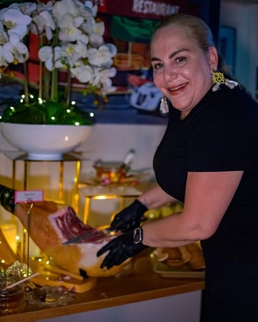 Chef profesional con guantes negros cortando una pierna entera de jamón ibérico en la mesa 