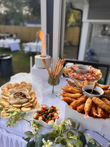 Buffet de aperitivos gourmet con camarones tempura, pan pita con hummus y cóctel de camarones frío.