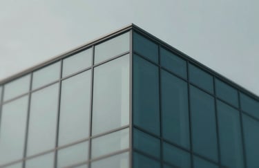 A professional and clean architectural detail of a modern building facade with sharp glass angles, symbolizing stability and legal structure. Palette includes shades of gray (#A0A0A0) and deep teal (#054D4B).