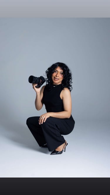 A smiling female photographer with curly hair holding a professional DSLR camera in a studio.