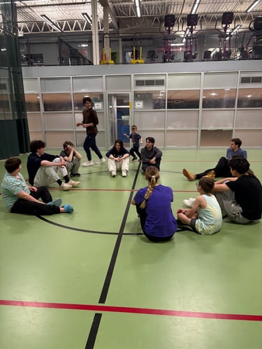 A group of children and volunteers sit to play an inclusive youth activity in a Kingston gymnasium