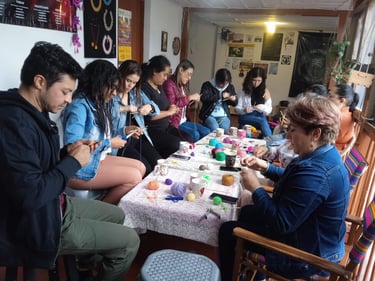 Personas concentradas al rededor de una mesa con hilos, herramientas y bebidas calientes, elaborando mandalas tejidos