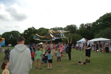 Excited children playing with giant soap bubbles during a summer outdoor festival in a park.