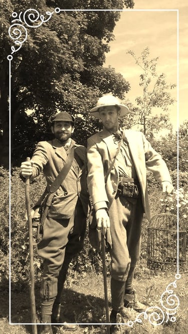 Two men in vintage steampunk explorer costumes posing outdoors with a pith helmet and birdcage.