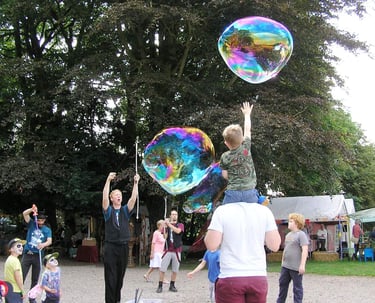 Young boy reaching for giant iridescent bubbles at an outdoor summer festival.