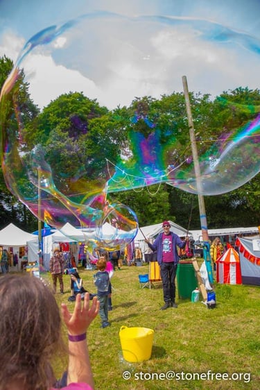 A street performer creates a giant iridescent soap bubble at an outdoor summer festival.