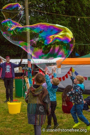 Excited children playing with giant rainbow soap bubbles at an outdoor summer festival.