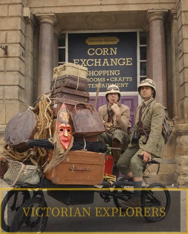 Victorian explorers in pith helmets sit on a bicycle piled with vintage luggage outside Doncaster Corn Exchange.