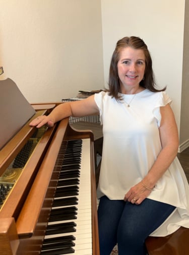 Smiling female piano teacher sitting at a classic brown upright piano for a music lesson.