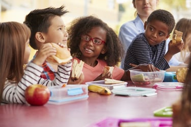 Visually impaired girl enjoying lunch and conversation with classmates in an inclusive school environment.