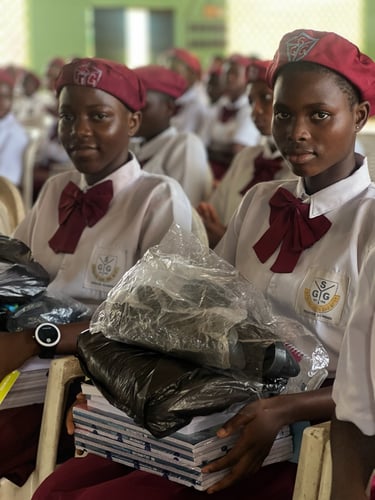 Students in red berets and white school uniforms holding educational supplies and books.
