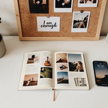 A creative vision board and open journal with photos on a white desk next to a smartphone.