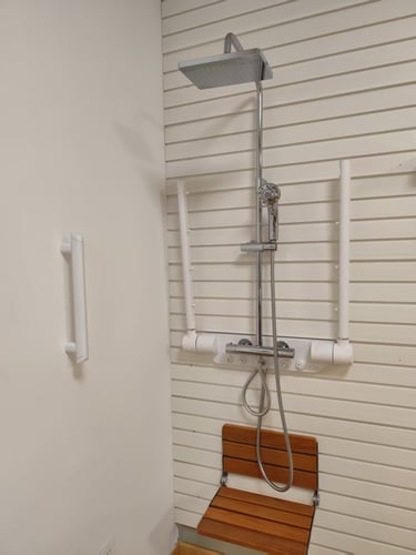Accessible shower featuring a rainfall shower head, safety grab bars, and a wall-mounted wooden folding seat.