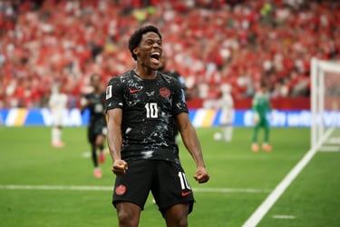 Canada soccer player Jonathan David celebrating a goal on the field in a black jersey.