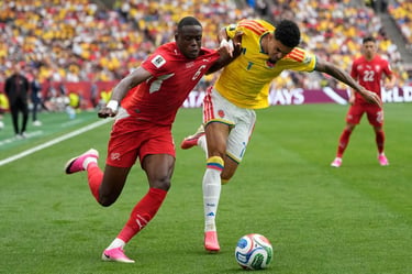 Two professional soccer players in red and yellow jerseys competing for a ball during an international match.