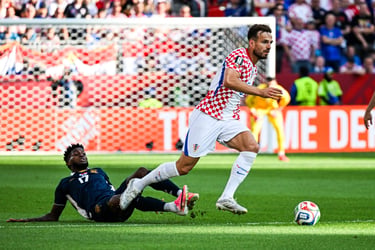 Croatia soccer player dribbles past a sliding defender during an intense international match.
