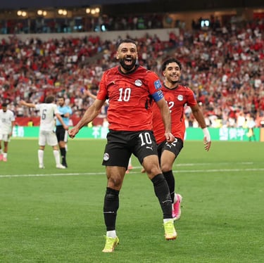 Egypt soccer player wearing a red jersey celebrates a goal on the field in a crowded stadium.