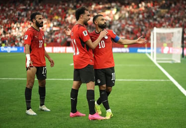 Egypt national football team players in red jerseys celebrating on a soccer field during a match.
