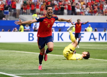 Spanish soccer player celebrates a goal on the field while the opposing goalkeeper lies on the grass.