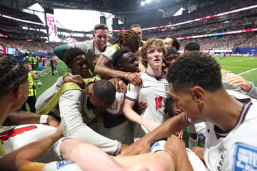 England football players celebrating a goal victory in a crowded soccer stadium during a major tournament.