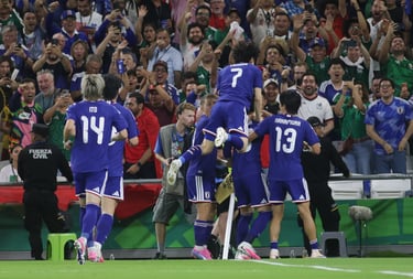 Japan national football team players in blue jerseys celebrate a goal in front of cheering fans.