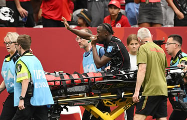 An injured soccer player waves to the crowd while being carried on a stretcher by FIFA medical staff.
