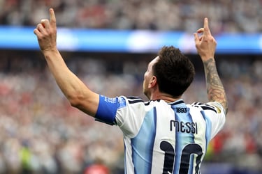 Lionel Messi celebrates a goal for Argentina, pointing both hands toward the sky in a stadium.