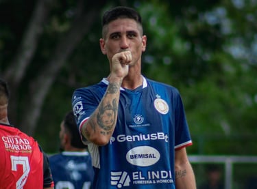 Professional soccer player in a blue jersey celebrating a goal with a kiss on his tattooed hand.