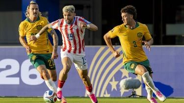 Paraguay and Australia national team players competing for the ball during a professional soccer match.