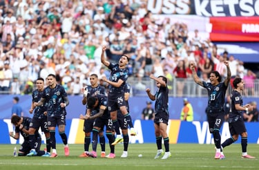 Professional soccer players in black jerseys celebrate a goal on the field in front of a crowded stadium.