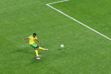 A soccer player in a yellow jersey kicks a ball on a green grass field near a white penalty line.
